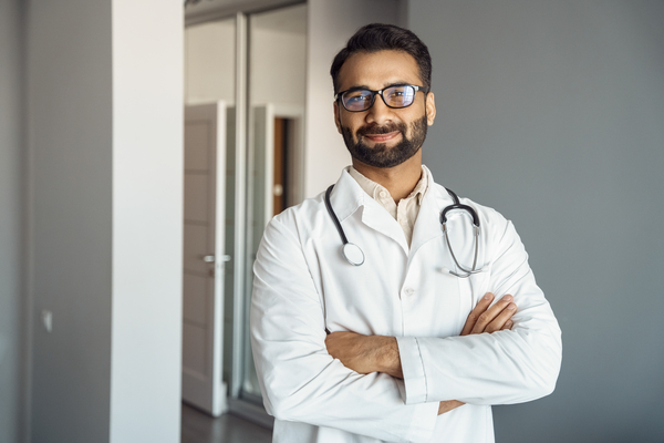 Portrait of male doctor wearing white lab coat, stethoscope standing and looking at camera in clinic hall. Arabian indian therapist, general practitioner headshot. 
